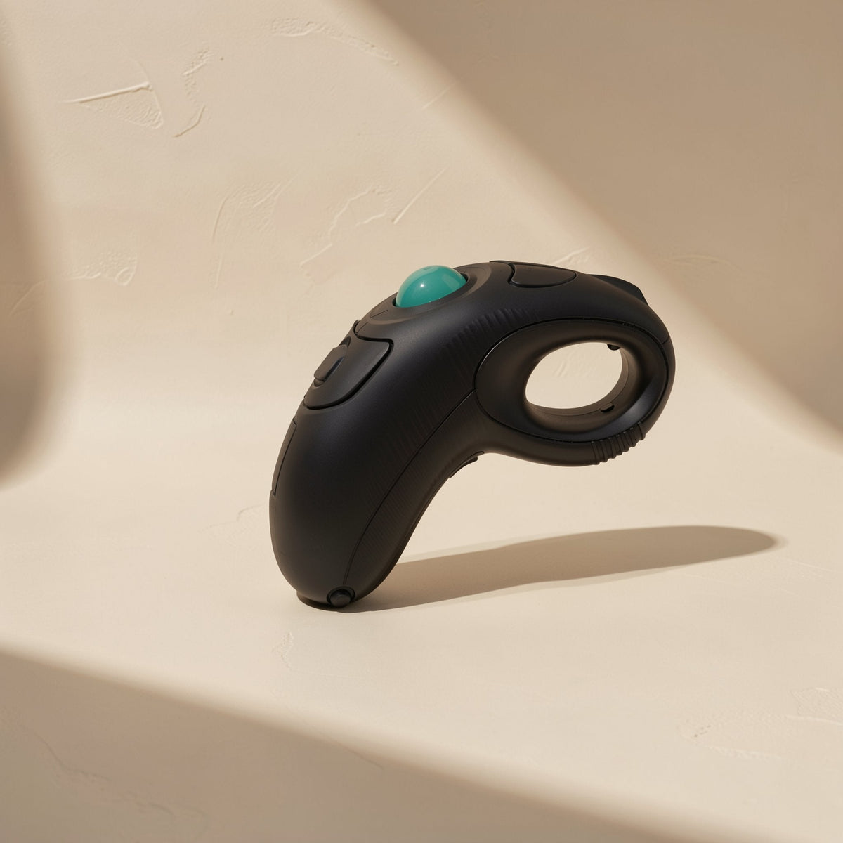 Ballroam – Side view of the black trackball mouse with finger loop and teal ball, standing upright in sunlight