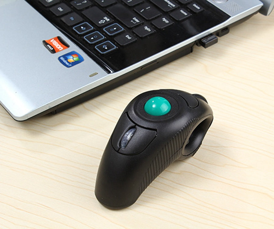 Orbitgrip Wireless Trackball Hand Grip Mouse beside a silver laptop on a wooden desk, USB receiver plugged in