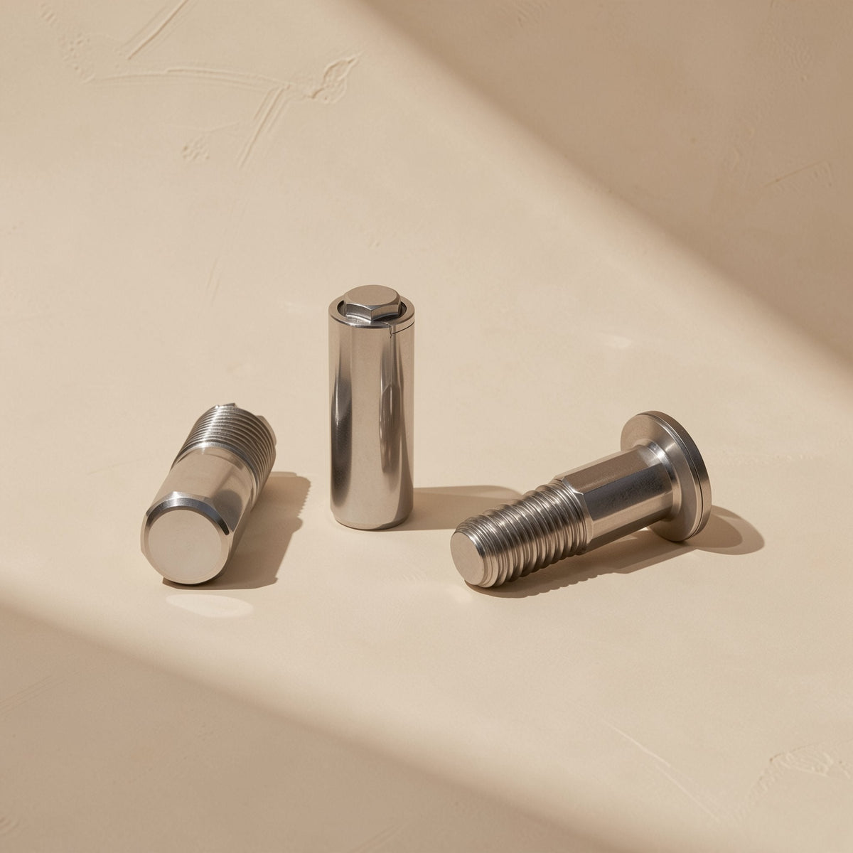 Hingehold Metric LCD Monitor Hinge Screw – three polished steel hinge screws, one standing upright, on a beige surface
