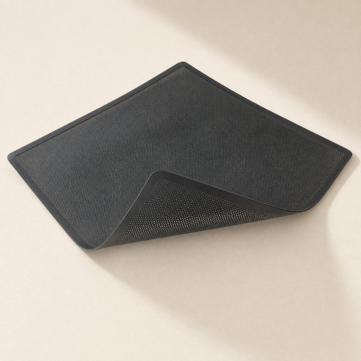 Magmesh – Flexible black filter net lifted at one corner, showing the mesh underside against a beige surface