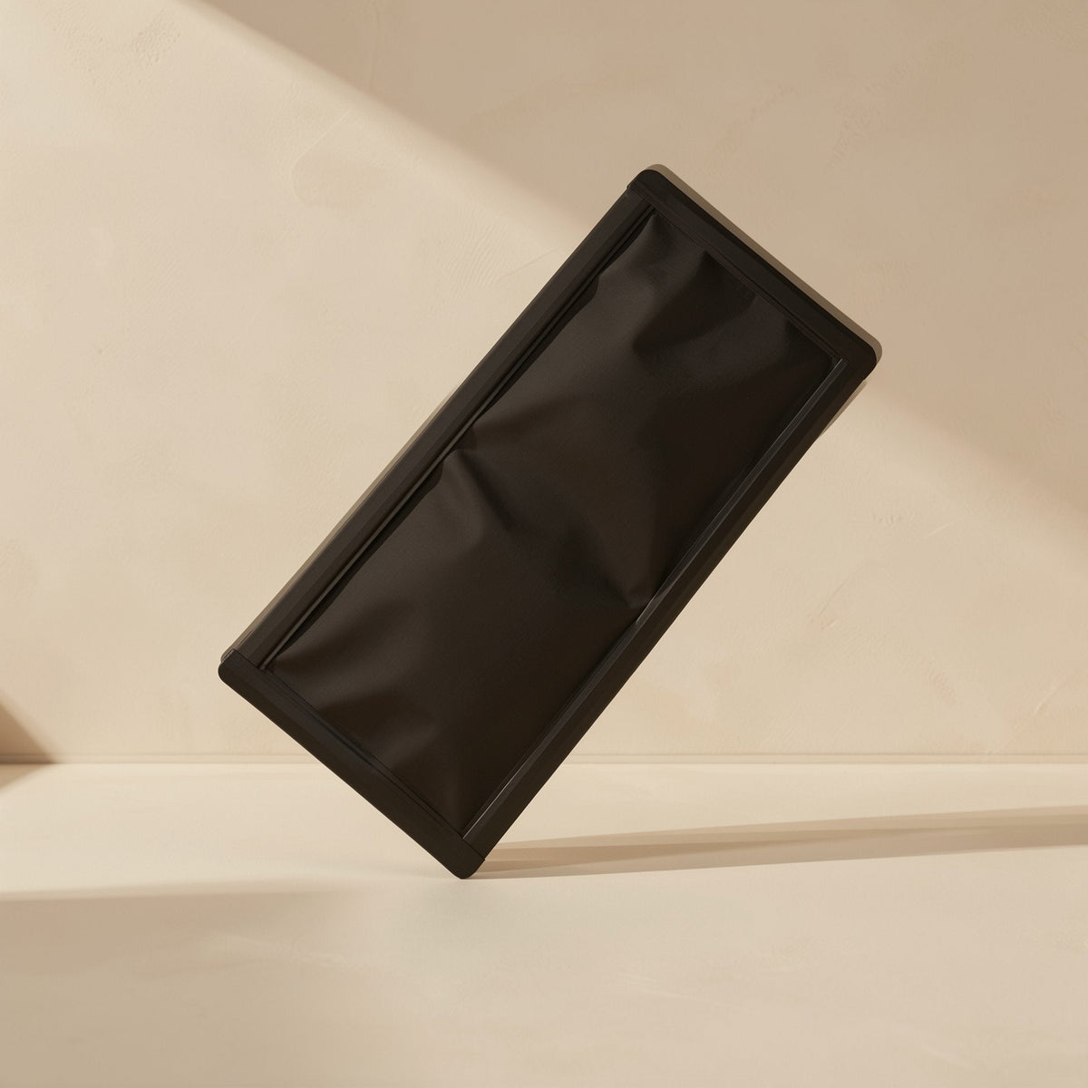 Dustmesh PVC magnetic dust filter in matte black, tilted upright against a warm beige wall