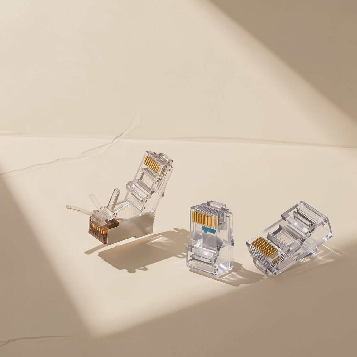 Cableclick – Three clear RJ45 connectors with gold pins, one with a metal shield, arranged in a beam of light