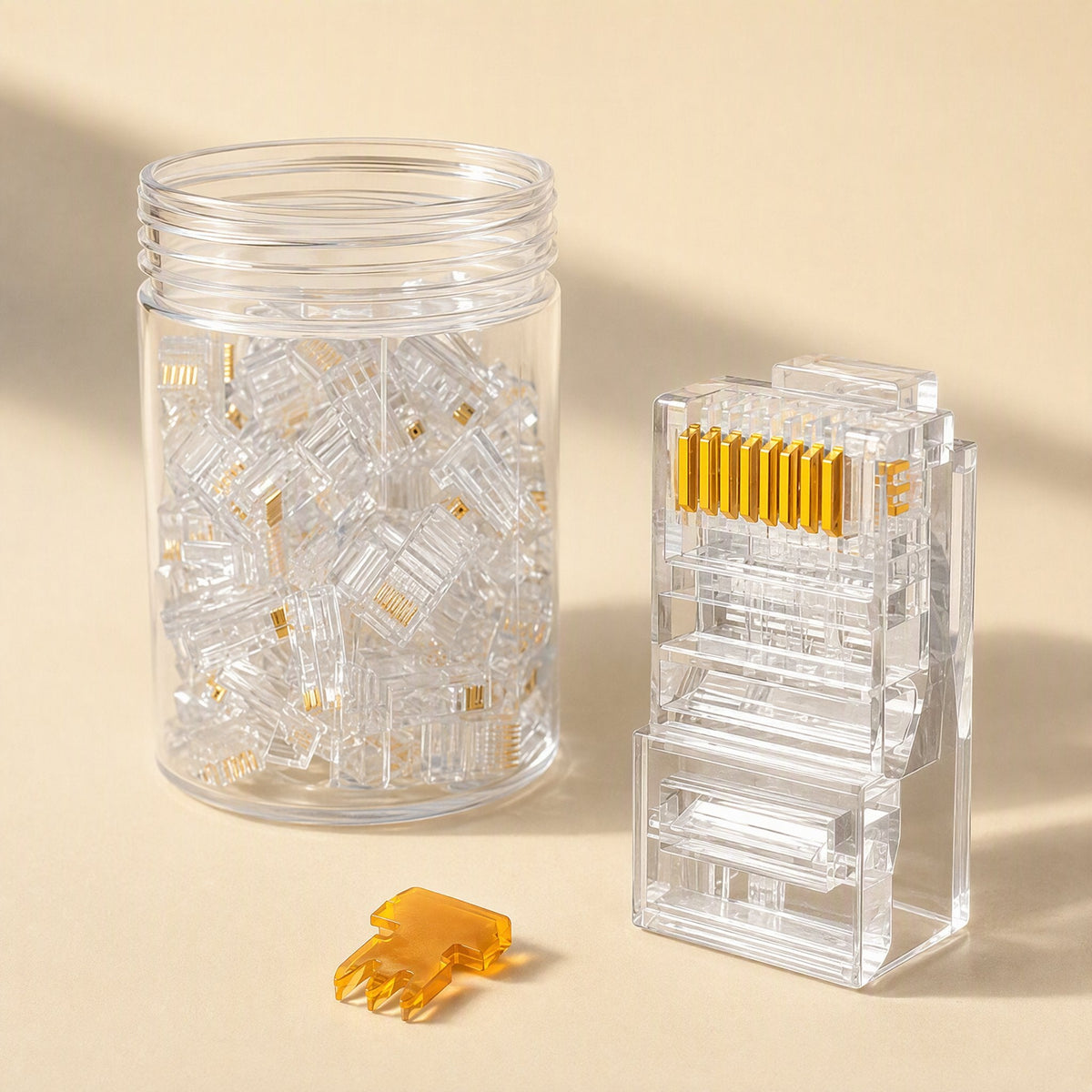 Netclick – Clear RJ45 connector with gold pins standing upright next to a jar of loose connectors and an orange part