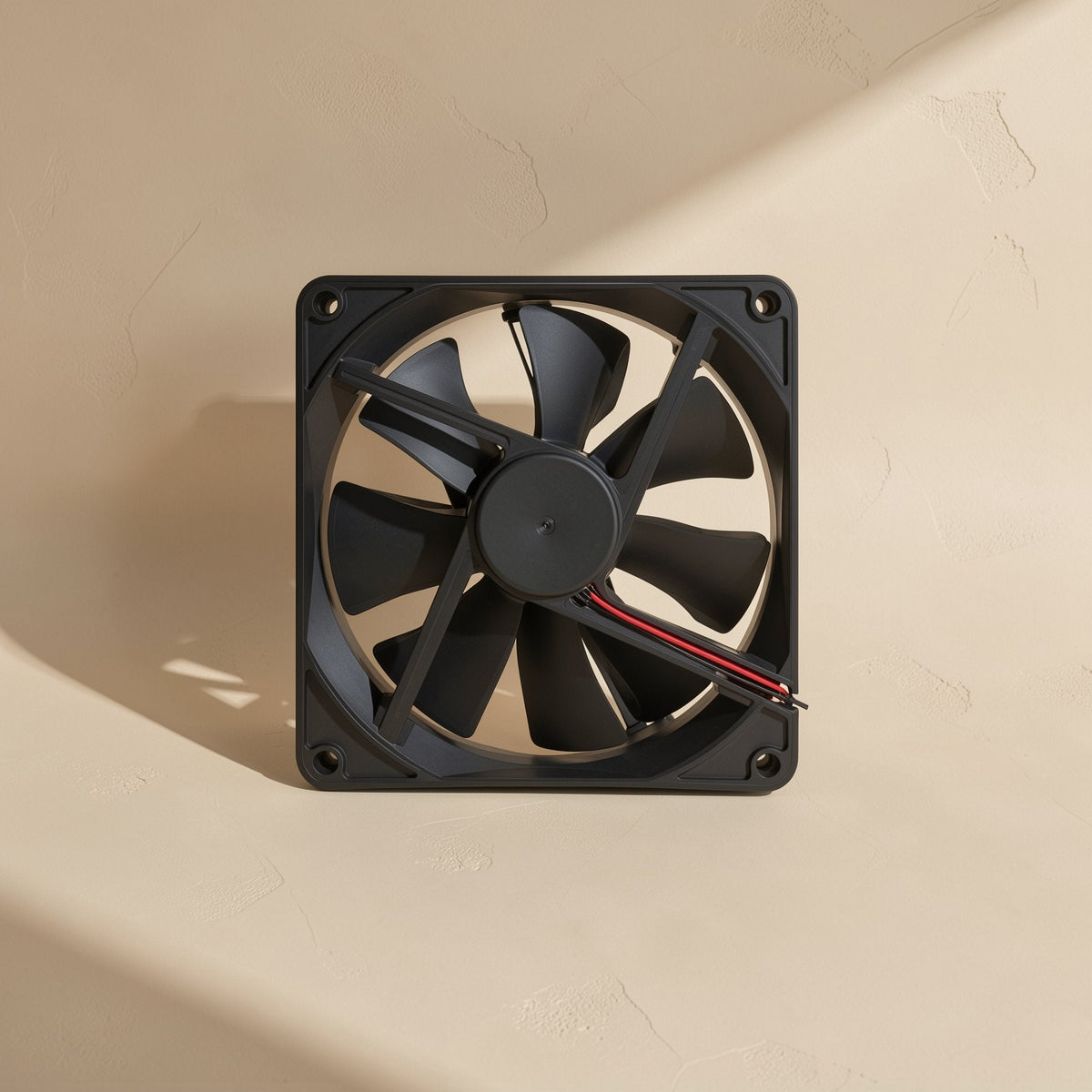 Bladechill – Black seven-blade cooling fan seen slightly from above, wires trailing from the hub on a plaster wall