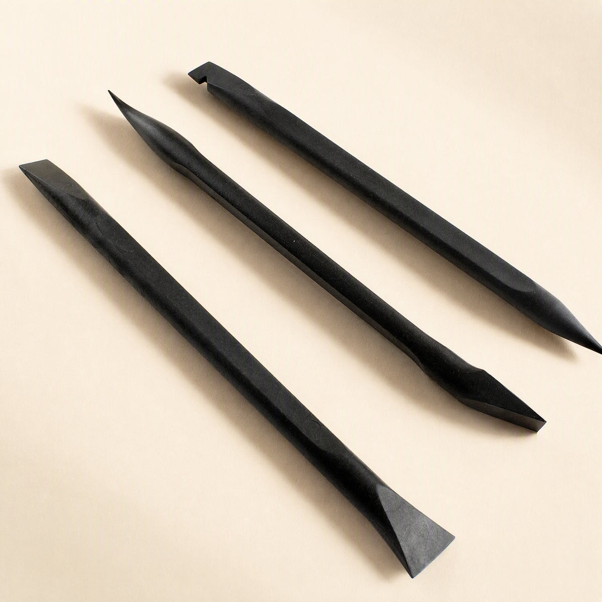 Prywise – Three black pry tools with flat, pointed and spade-shaped ends laid diagonally on a cream surface