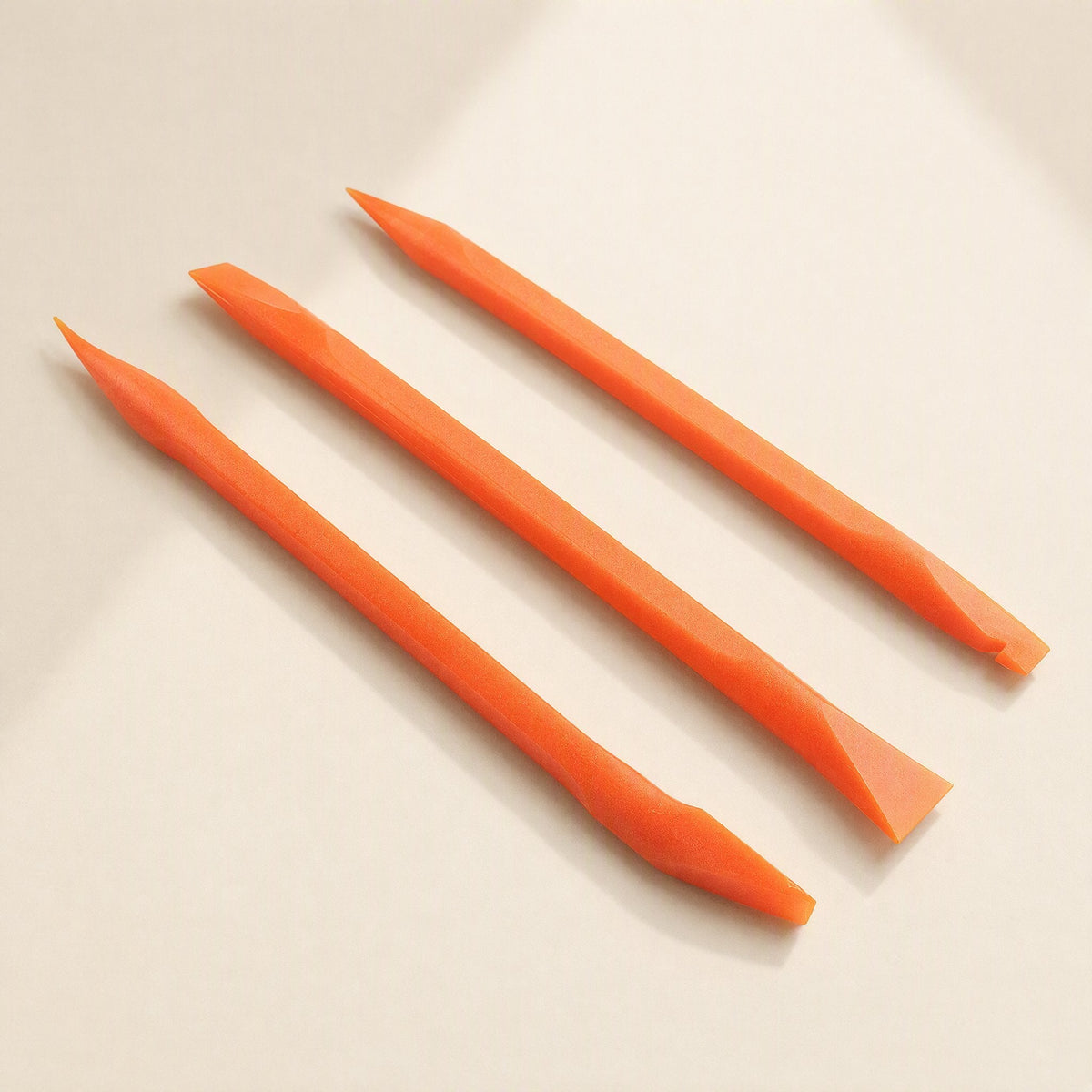 Prywise – Three orange pry tools with pointed and chisel tips arranged side by side on a soft beige backdrop