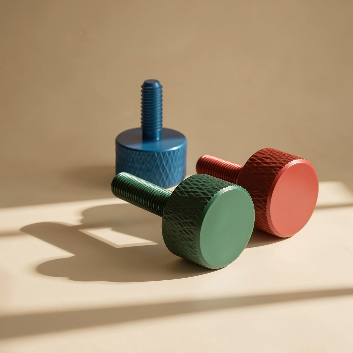 Gripturn – Three anodized thumb screws in blue, green and red casting shadows on a warm tan background