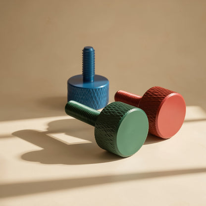 Gripturn – Three anodized thumb screws in blue, green and red casting shadows on a warm tan background