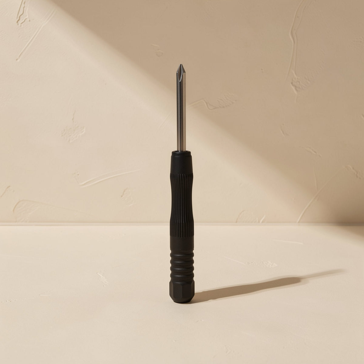 Screwbit – Single black screwdriver with ribbed handle standing upright, steel tip pointing up, casting a long shadow