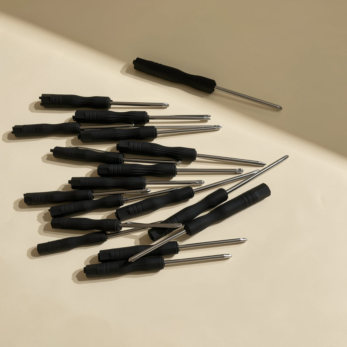Screwbit – Pile of black screwdrivers with steel shafts scattered across a beige surface in angled light