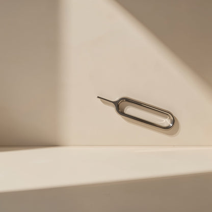 Screwbit – Slim metal SIM card ejector pin with an oval loop lying on a cream surface in soft shadow