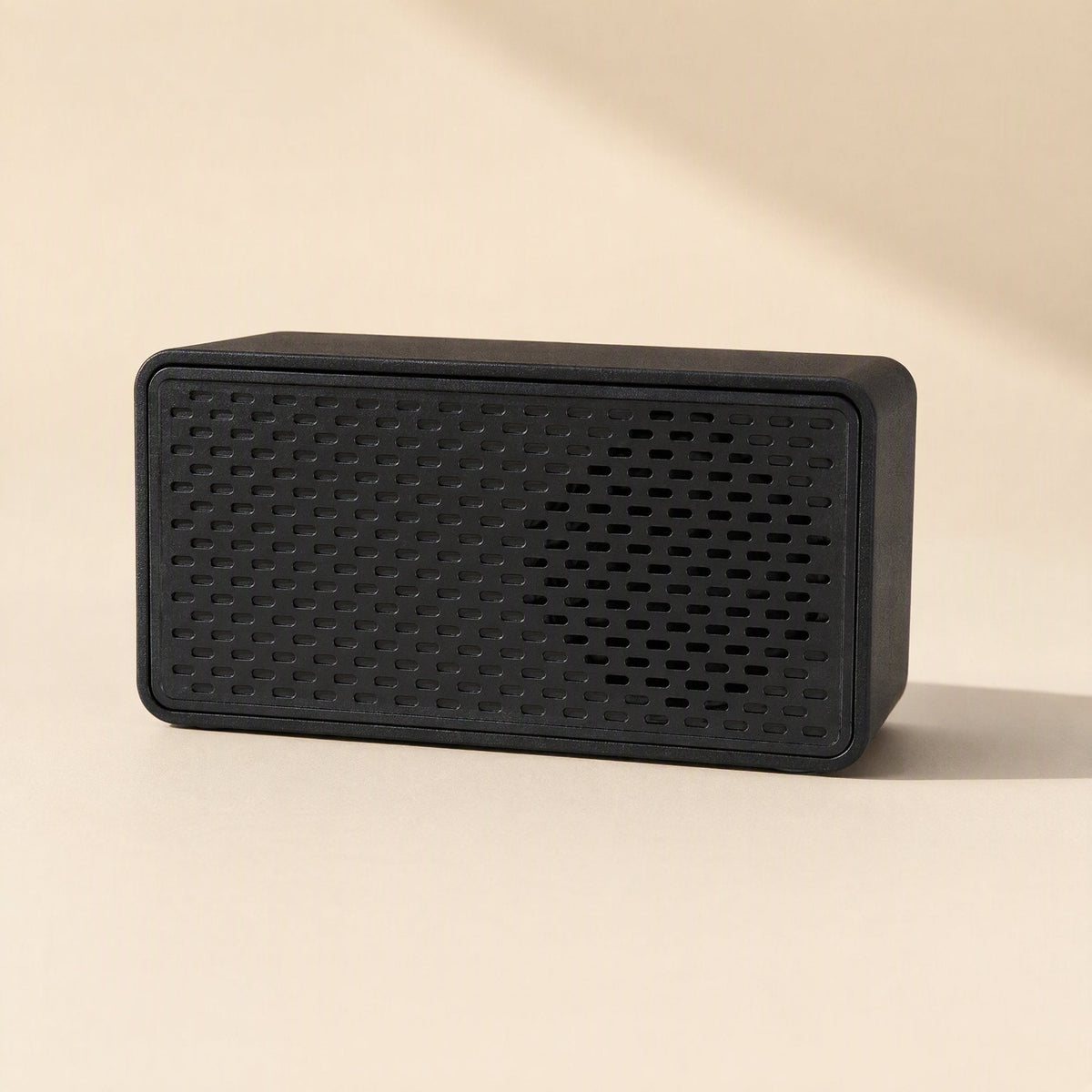 Soundport – Black rectangular speaker with slotted front grille on a cream background, front view with soft shadow