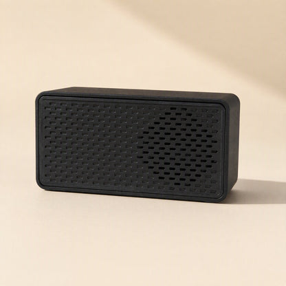 Soundport – Black rectangular speaker with slotted front grille on a cream background, front view with soft shadow