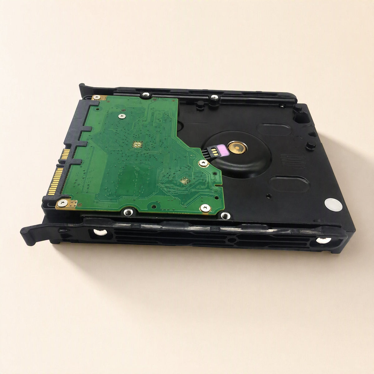Coolbrace – Underside of a 3.5-inch hard drive clamped between black rails, green circuit board and connector showing