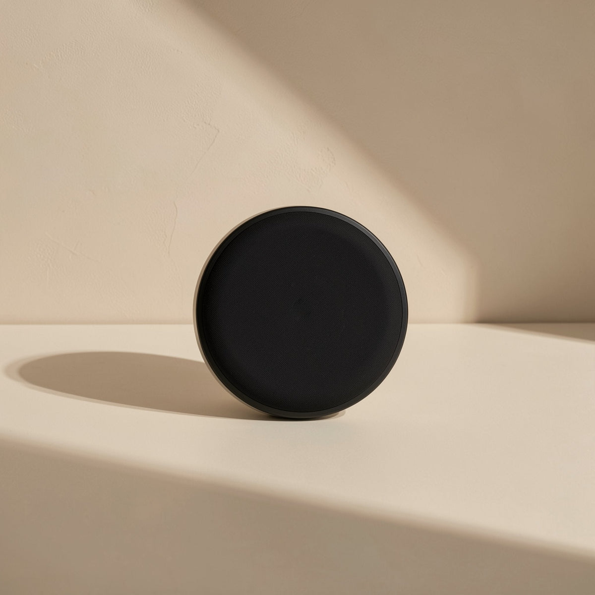 Voltflow Wireless Charger – back of the round black charger standing on a cream ledge, casting a long shadow on a beige wall