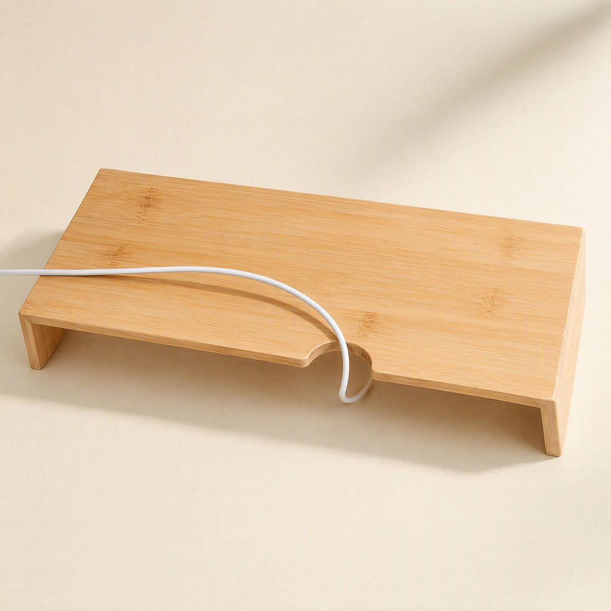 Bamboorise – Top-down view of a bamboo monitor stand with a curved cable notch and a white cable looped through it