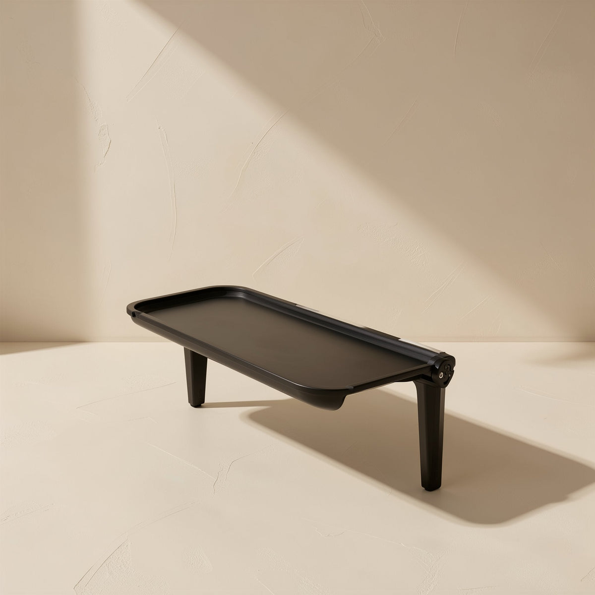 Screenstash Monitor Stand Storage Rack, black shelf with two legs, side view on a cream surface
