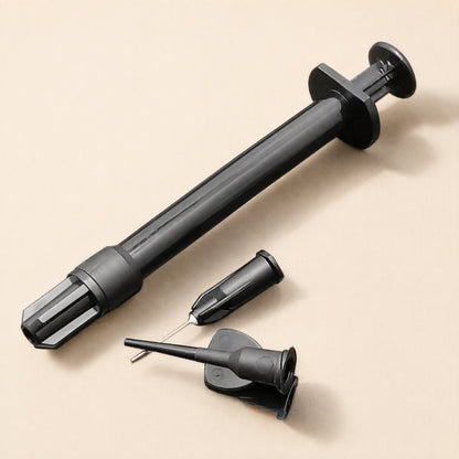 Meltlink – Black syringe laid diagonally beside a needle tip with cap and a second angled tip, on a beige surface