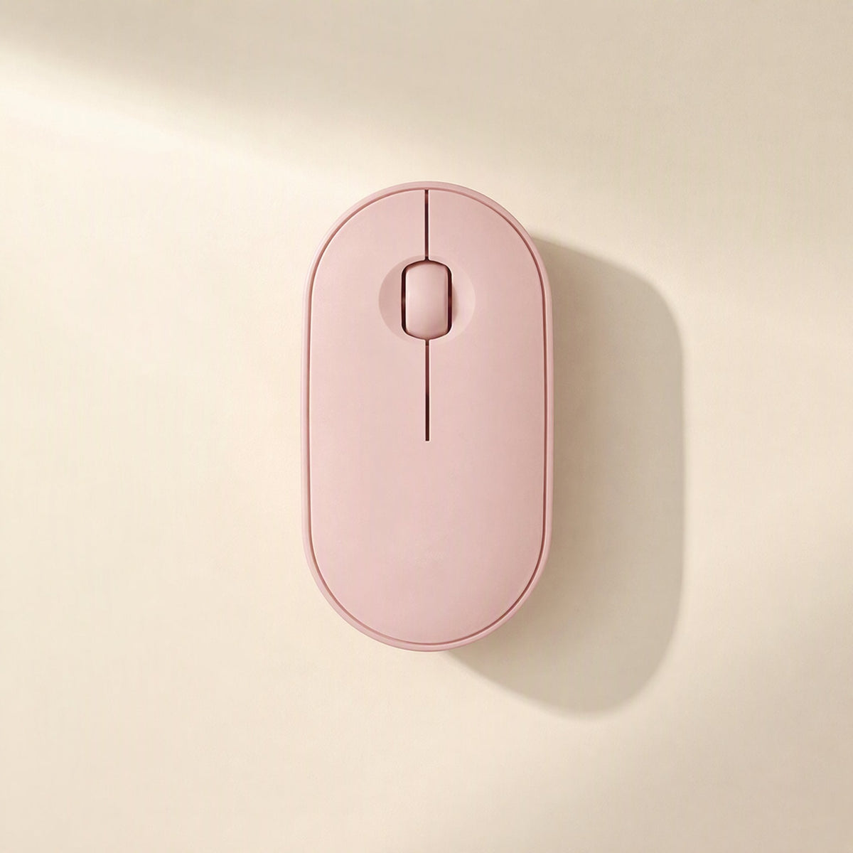 Quietcursor – Pink wireless mouse shown top-down, with a rounded oval body and scroll wheel, in warm sunlight