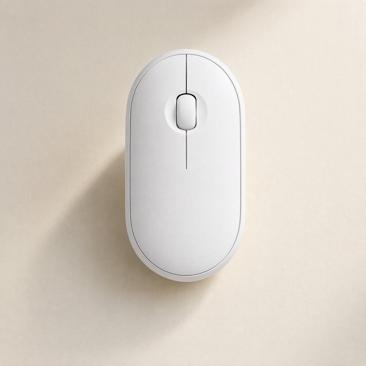 Quietcursor – Top view of a white wireless mouse with a slim centre line and scroll wheel, on a beige surface