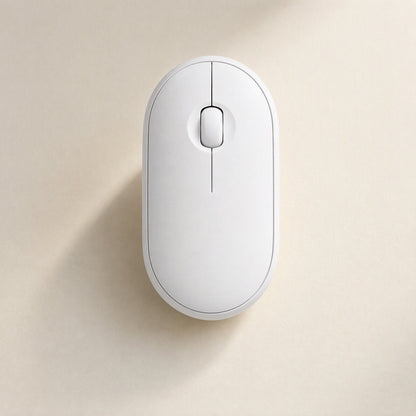 Quietcursor – Top view of a white wireless mouse with a slim centre line and scroll wheel, on a beige surface