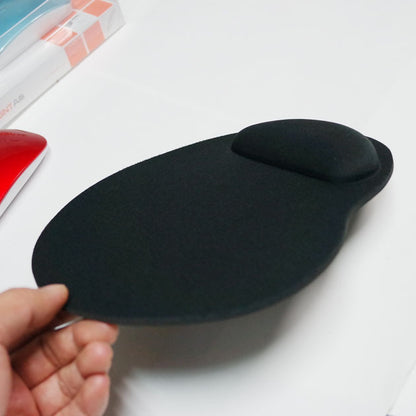 Softtrack – Hand holding the black pad at an angle to show the raised wrist rest, with boxes and a red mouse behind