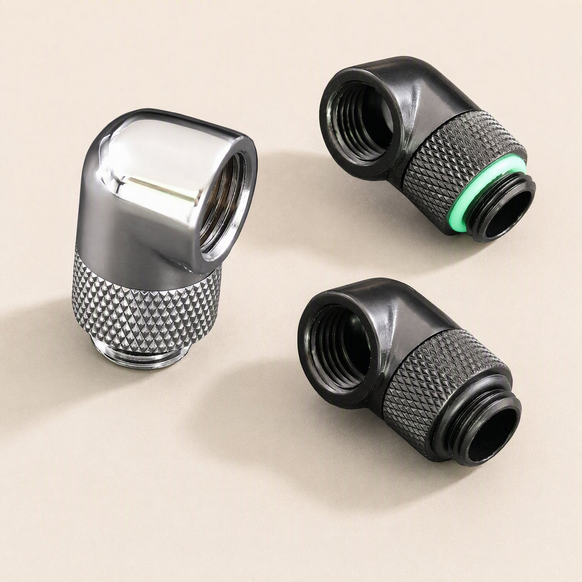 Swivelbend 360° Rotating Water Cooling Elbow in chrome and two in black, one with a green O-ring, on beige