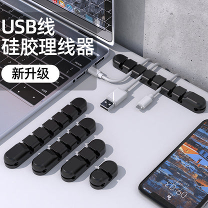 Wirenest Silicone Data Cable Organizer Clip in black, four sizes arranged beside a laptop and phone