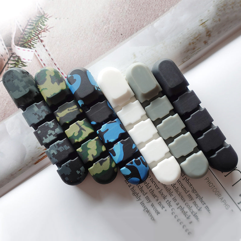 Wirenest – Six cord clips in a row in camouflage, blue, white, grey and black colours on a printed paper background