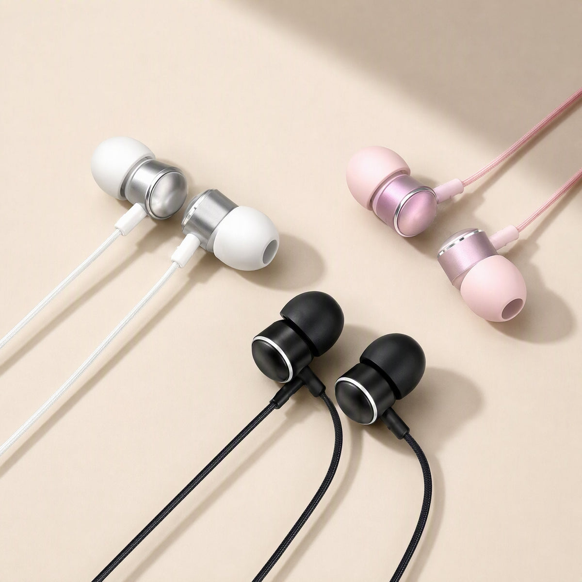 Earchime – White, rose pink and black wired in-ear headphones with metal-ringed earbuds arranged on a beige backdrop