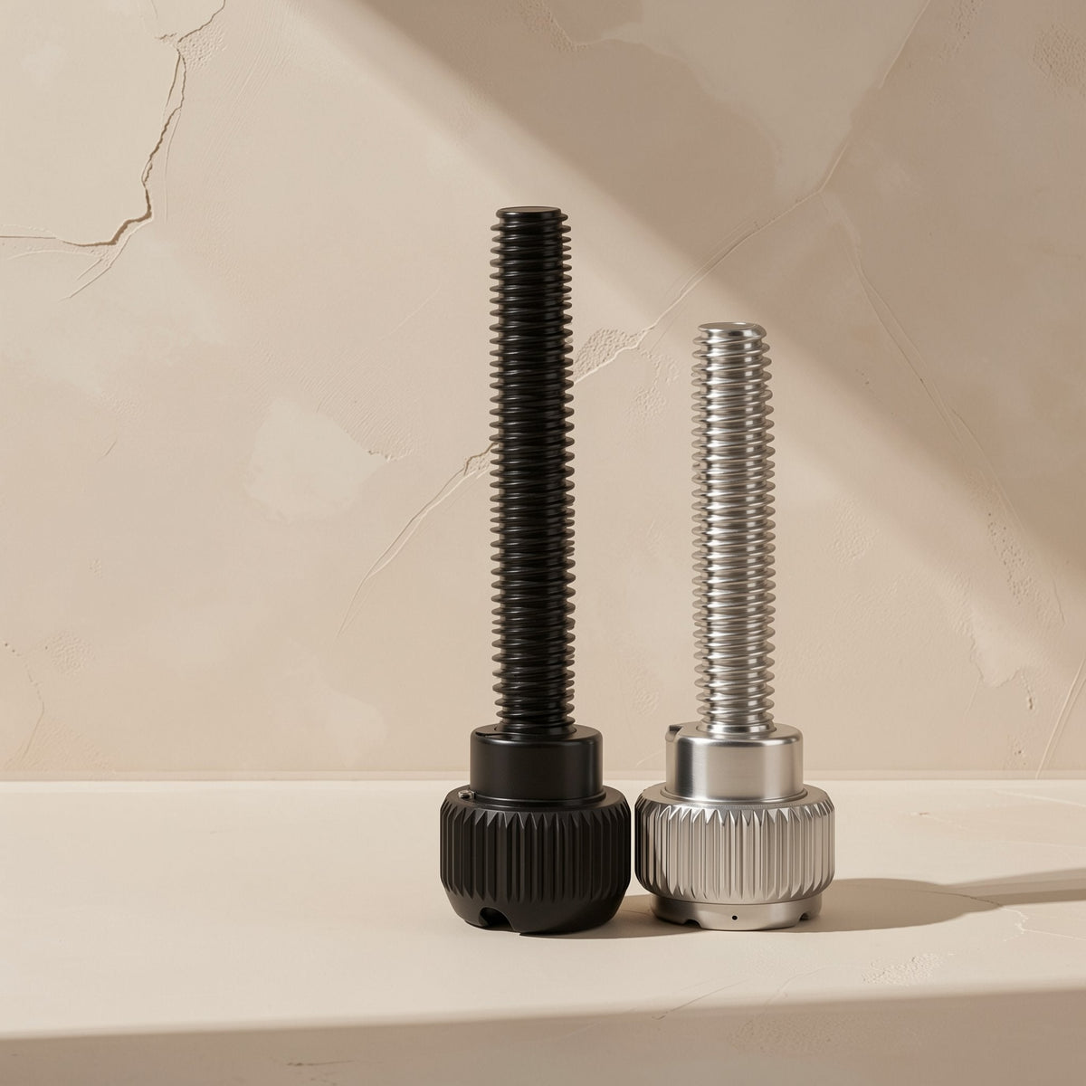 Casebolt – Black and nickel-plated knurled thumb screws standing side by side against a beige wall