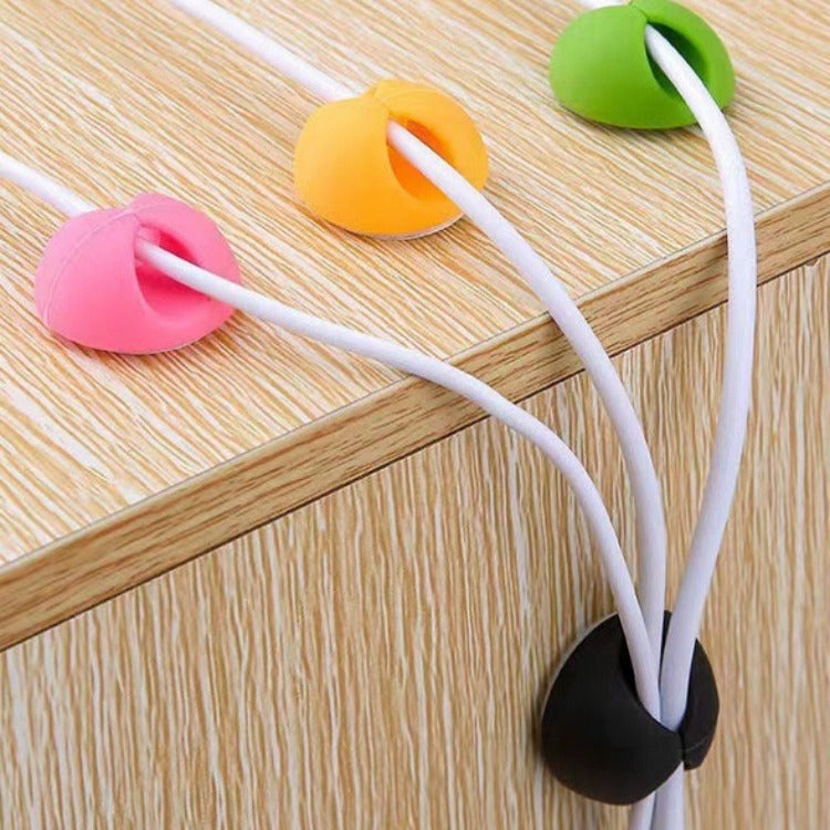 Cordscape TPR Desktop Cable Organizer clips in pink, orange, green and black holding white cables on a desk edge