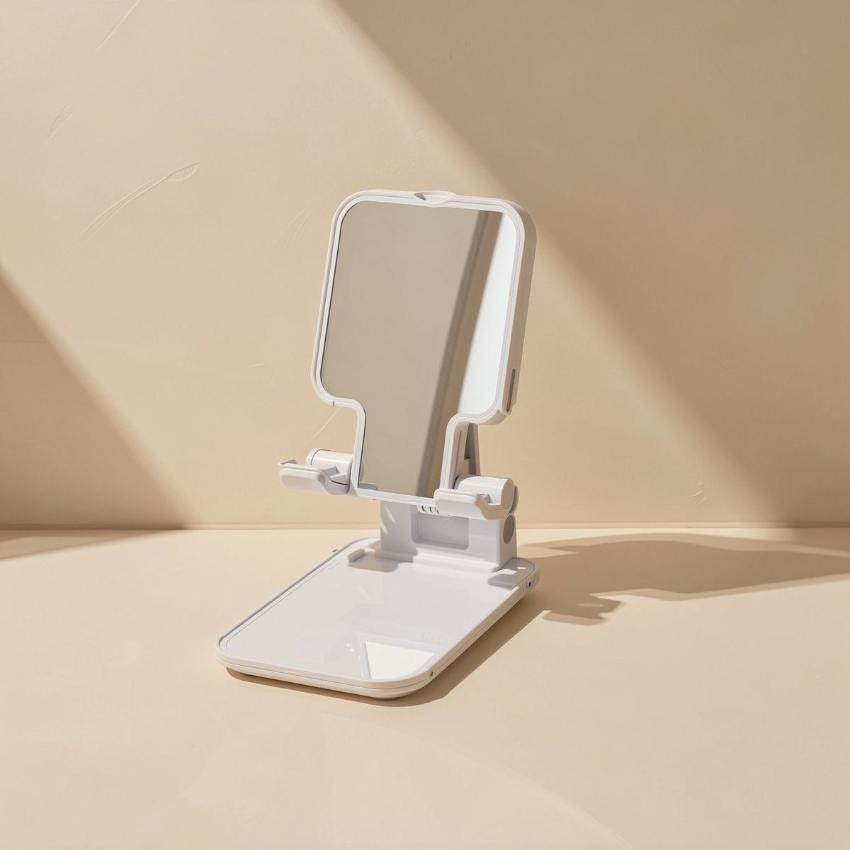 Foldperch Foldable Adjustable Phone Stand – white phone stand with a mirrored face plate, open and angled on a beige tabletop