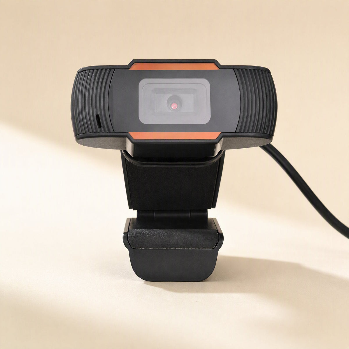 Clearcam – Front view of the webcam with its lens, ribbed sides and attached USB cable, standing on its clip base