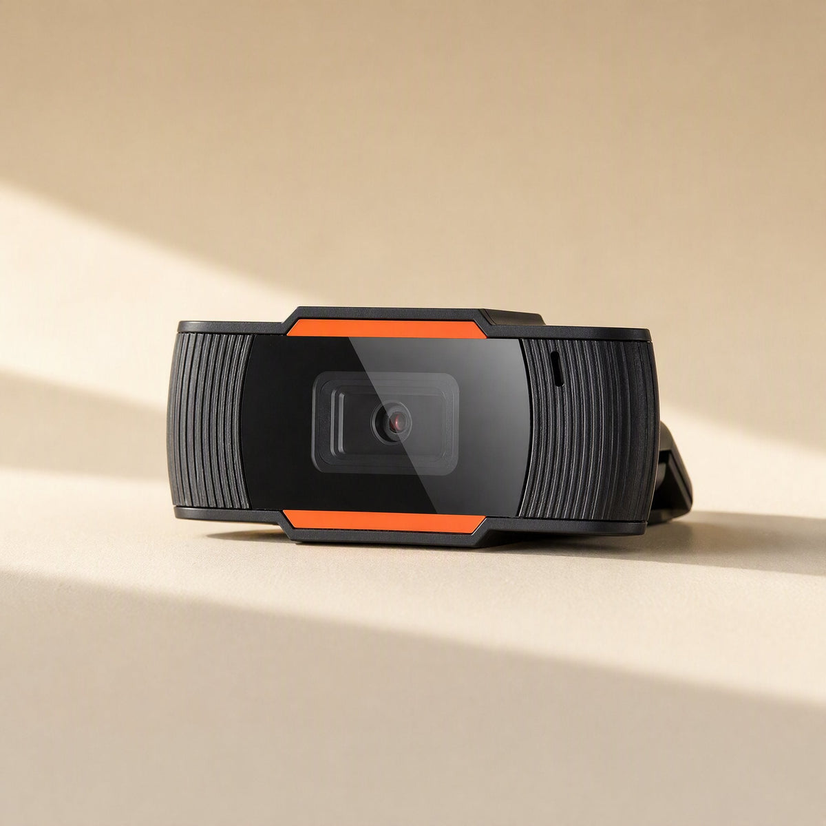 Clearcam – Close-up of the camera lying flat, showing the lens, orange trim and ribbed grip in striped sunlight