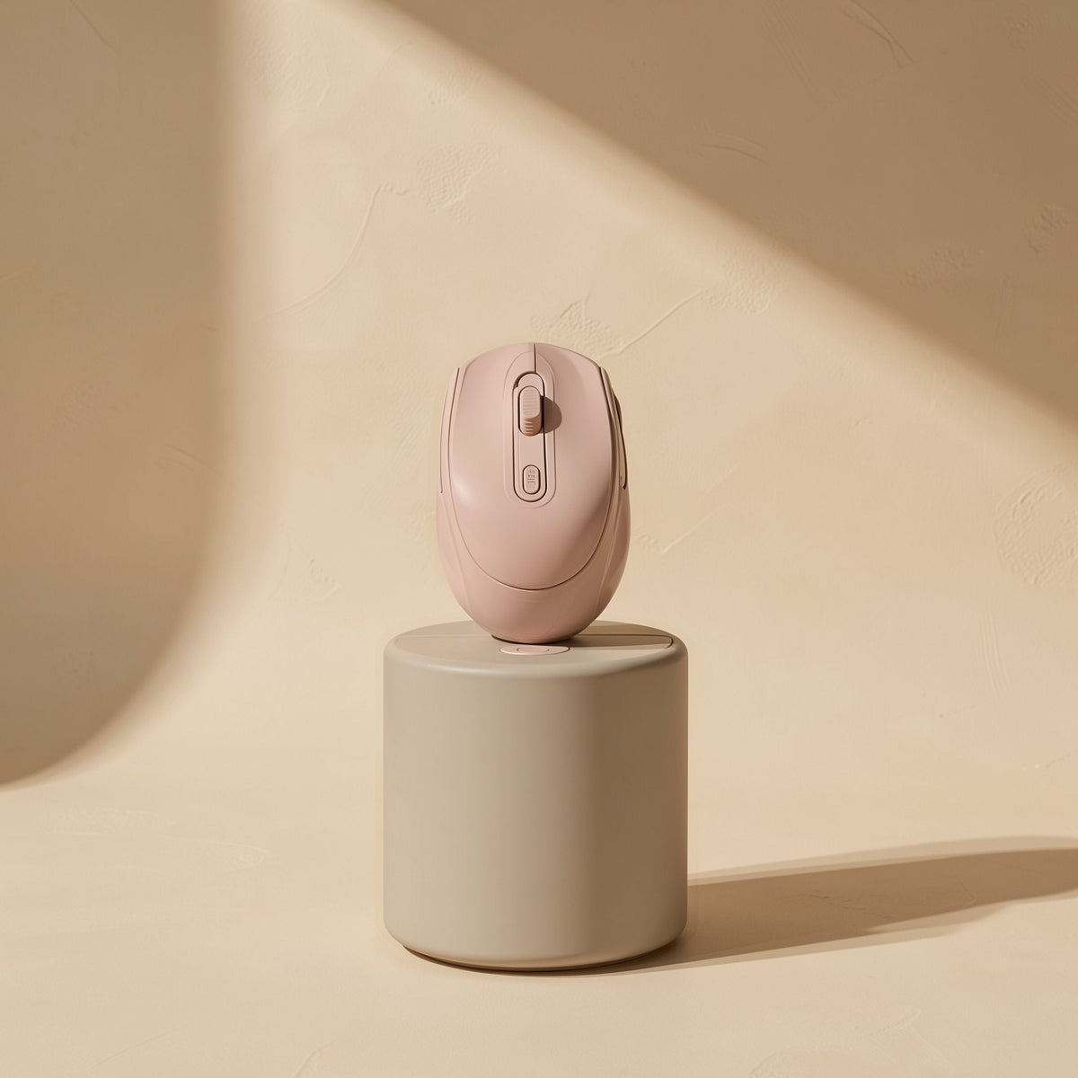 Opticlick – Blush pink wireless mouse standing upright on a grey cylindrical pedestal against a sunlit beige wall