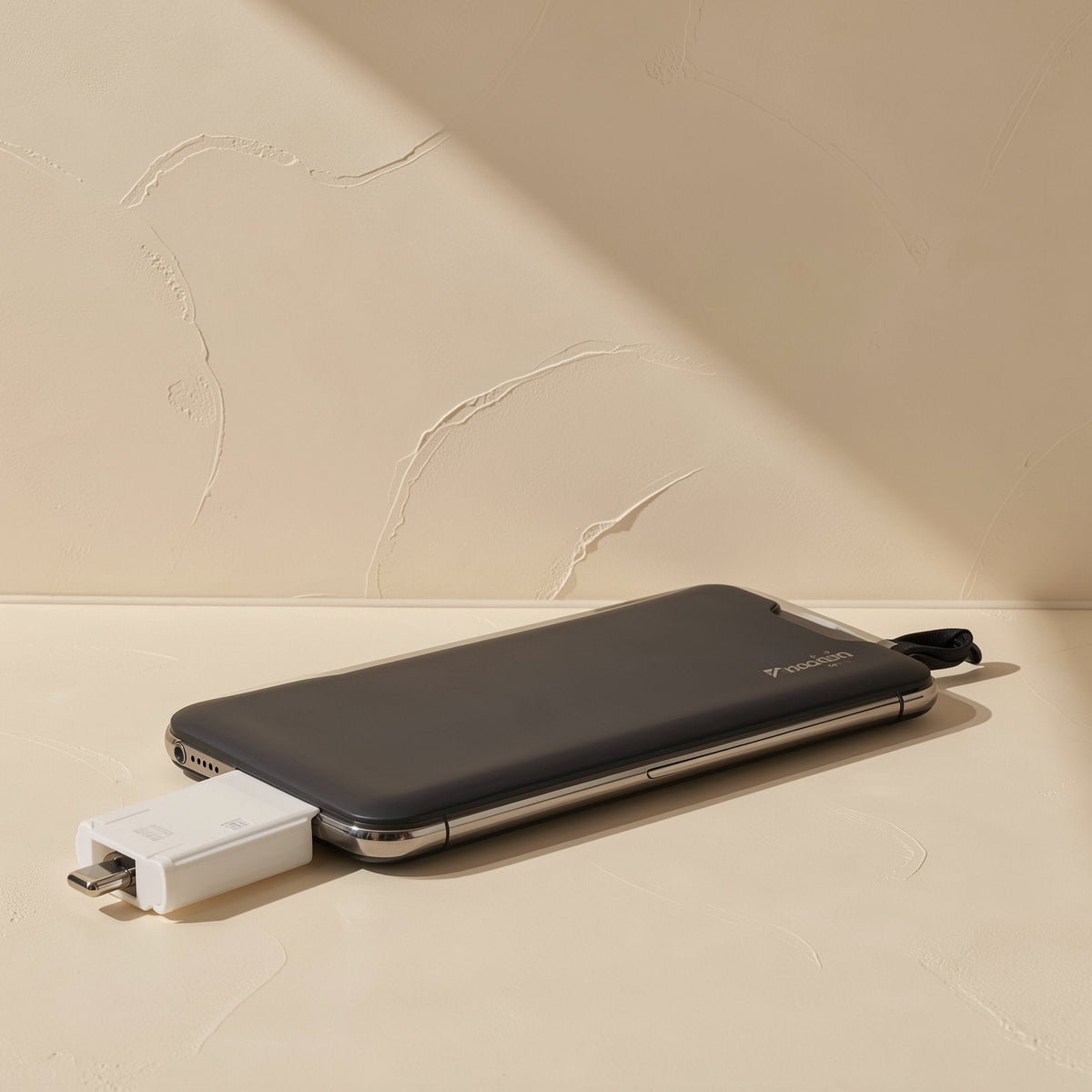 Sixport Type-C Six-in-One Card Reader – white card reader plugged into the bottom of a smartphone lying on a beige surface