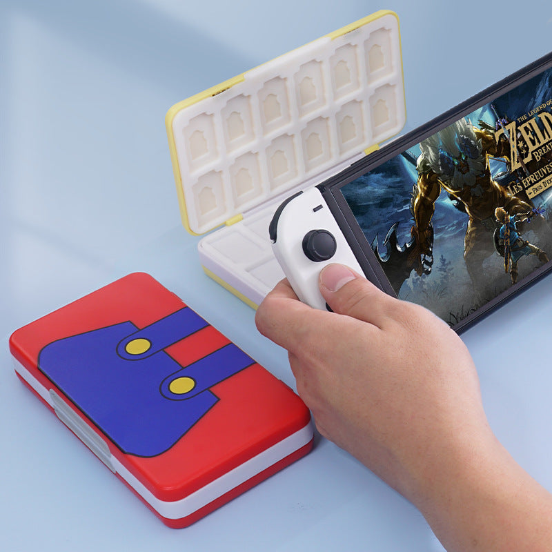Tuckbox – Red and blue overalls-design case lying shut beside a hand holding a Switch playing Zelda, with open case behind