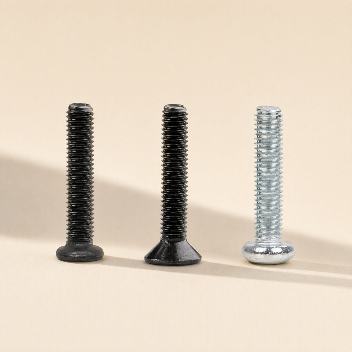 Microbite – Three black and silver machine screws with pan, flat and countersunk heads standing upright on a cream background