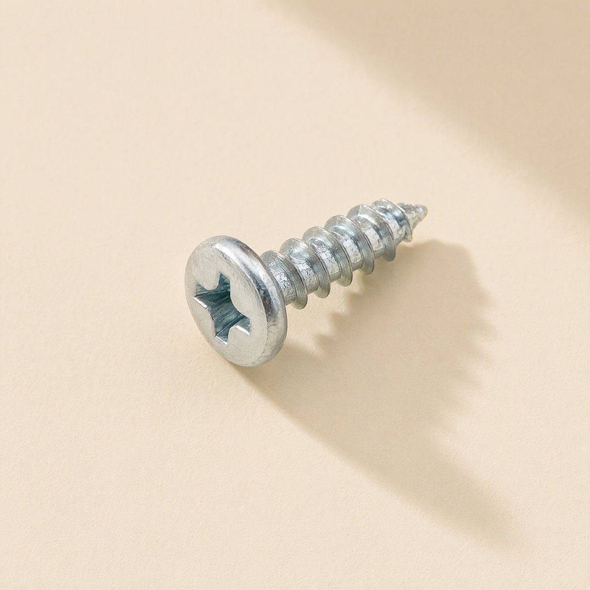 Microbite – Close-up of a single zinc-plated cross-head self-tapping screw with a rounded head, lying on its side