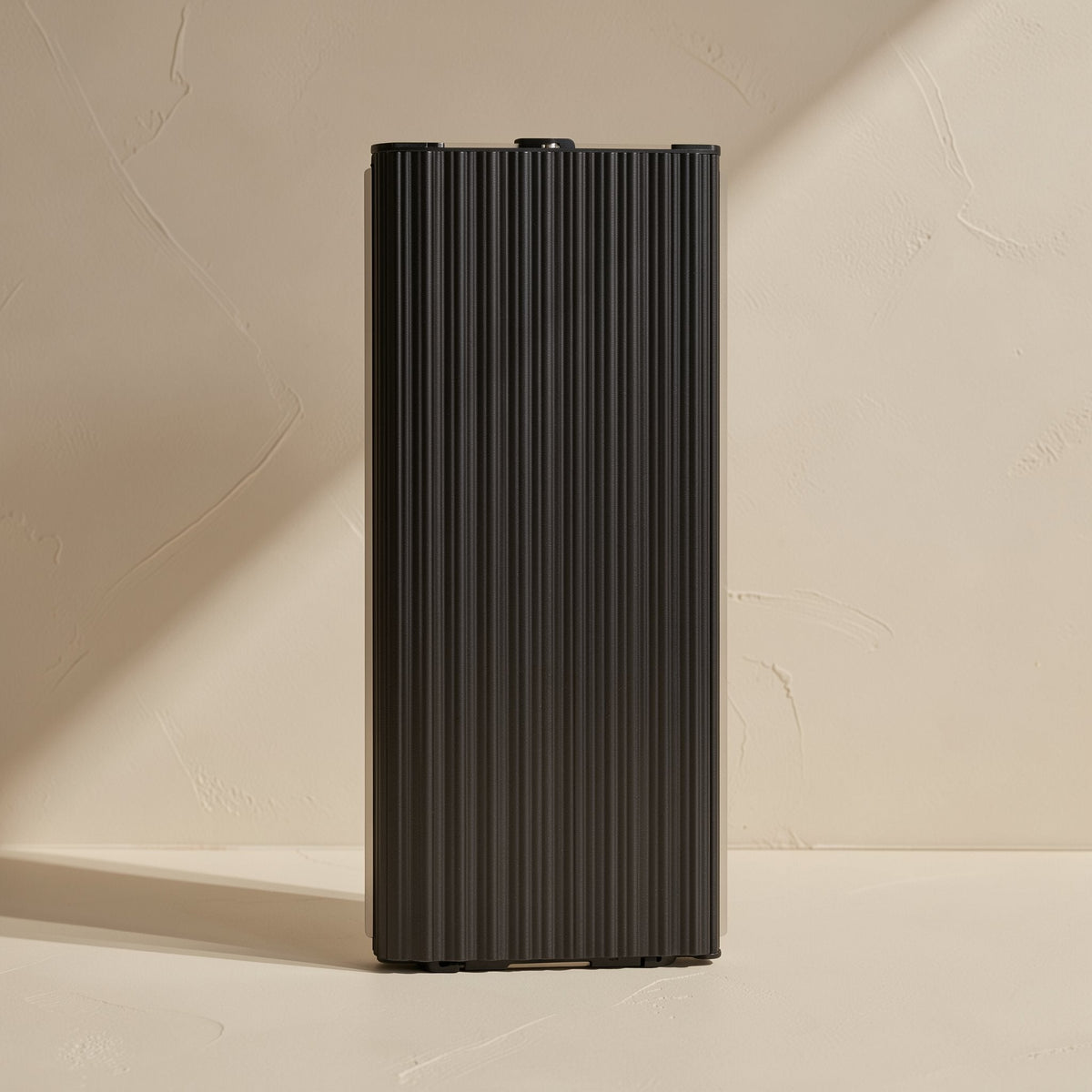 Swiftbyte – Black ribbed metal portable SSD standing upright against a textured beige wall in angled sunlight