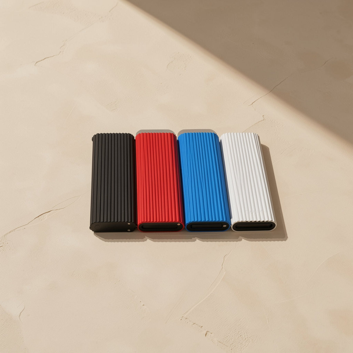 Swiftbyte – Black, red, blue and white ribbed portable SSDs lying in a row on a cracked beige surface, ends facing front