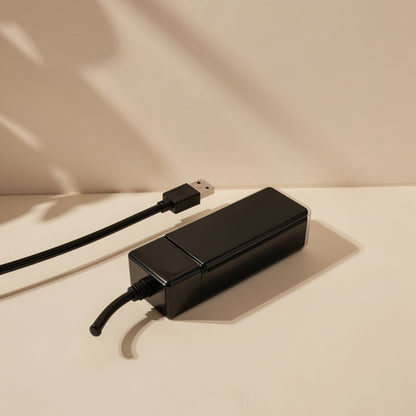 Portsplit – Black hub lying on a beige surface with its cable looped and a USB plug at the far end, with soft shadows