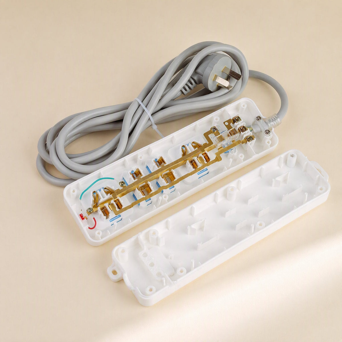 Cordcraft – Open power strip showing brass internal contacts and wiring beside the detached white cover and coiled grey cord