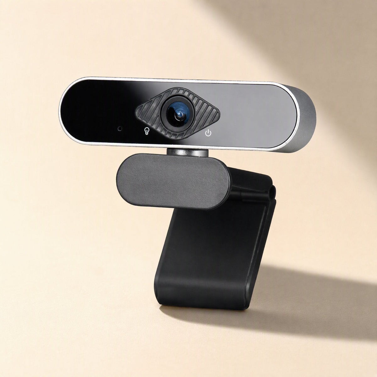 Faceview – Webcam tilted slightly to the right on its black clip stand, with soft diagonal shadows on a cream surface