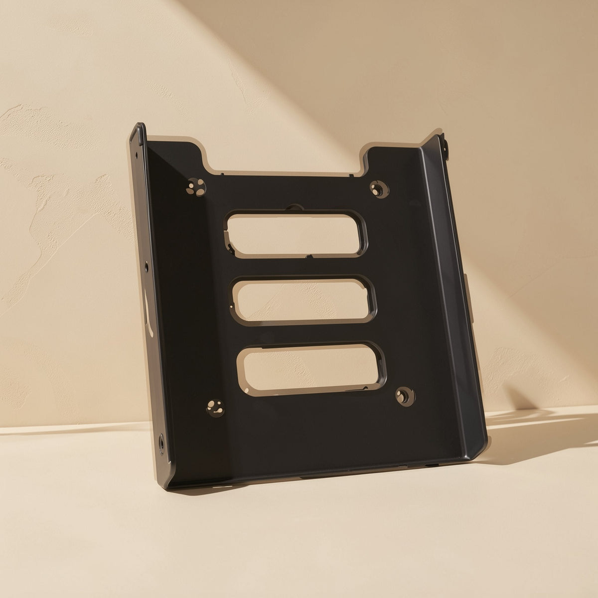 Diskcradle – Front view of the black metal bracket standing upright, showing three slotted cutouts and four mounting holes