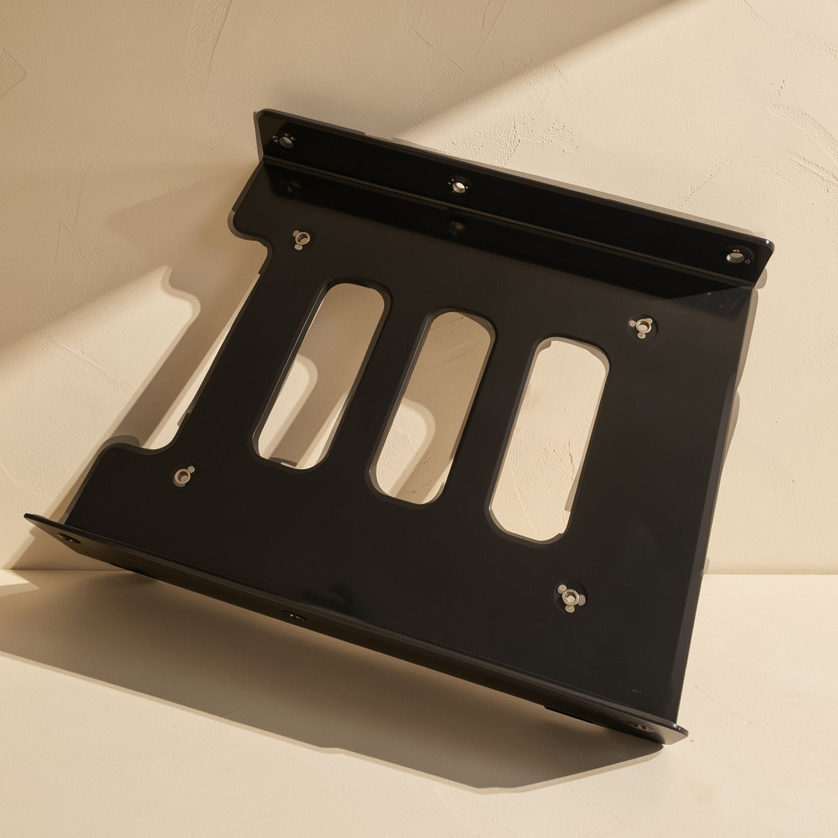 Diskcradle – Black bracket lying at a diagonal, showing slotted cutouts, screw holes and the angled mounting flange