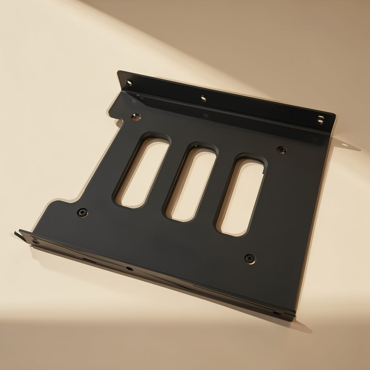 Diskcradle – Top-down view of the black metal bracket on a cream surface, showing slots and screw holes along the edges
