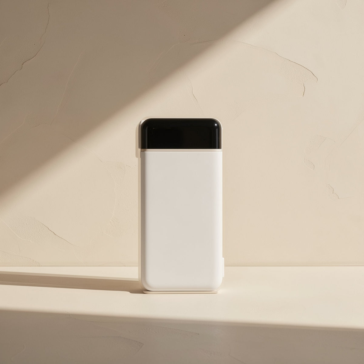 Quickvolt – White power bank with a black glossy top panel, front view against a cream wall in angled sunlight