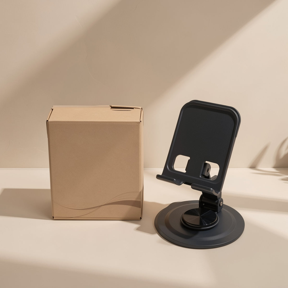 Foldmate Foldable Metal Phone Stand in black with a round swivel base beside a kraft cardboard box
